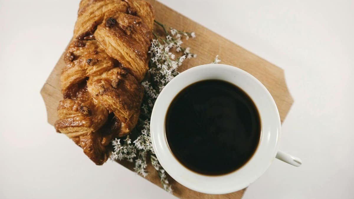 A cup of black coffee and flaky croissant on a wooden board, perfect breakfast setup.