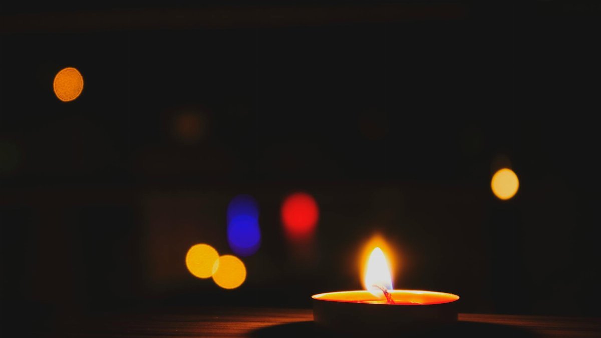 A candle glows warmly in the foreground against a bokeh-filled dark background.
