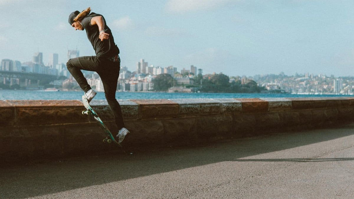 Energetic skateboarder performing tricks near a city waterfront with a clear sky backdrop.