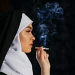 Profile of a nun in traditional habit smoking a cigarette, with smoke swirling against a dark backdrop.