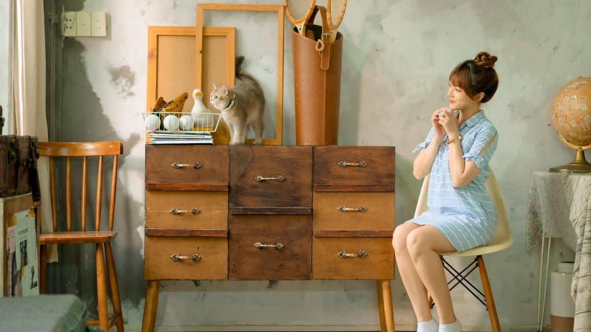 A cozy indoor scene featuring a woman sitting next to a cabinet with a cat on top.