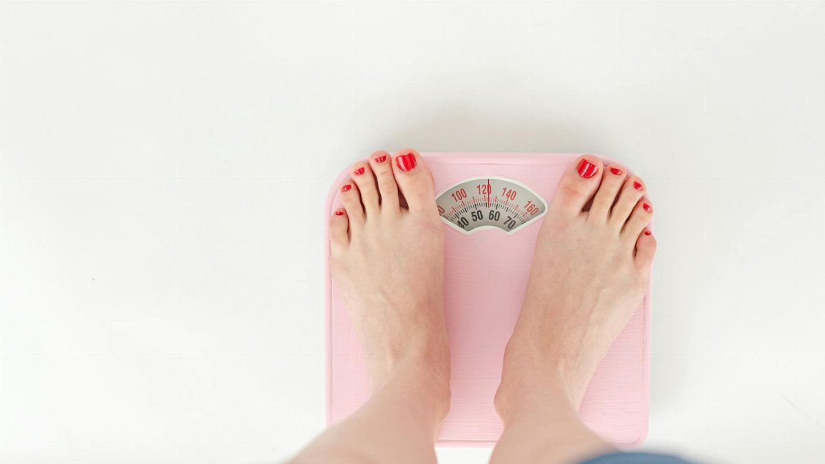 Top view of crop anonymous barefoot female measuring weight on scales on white background
