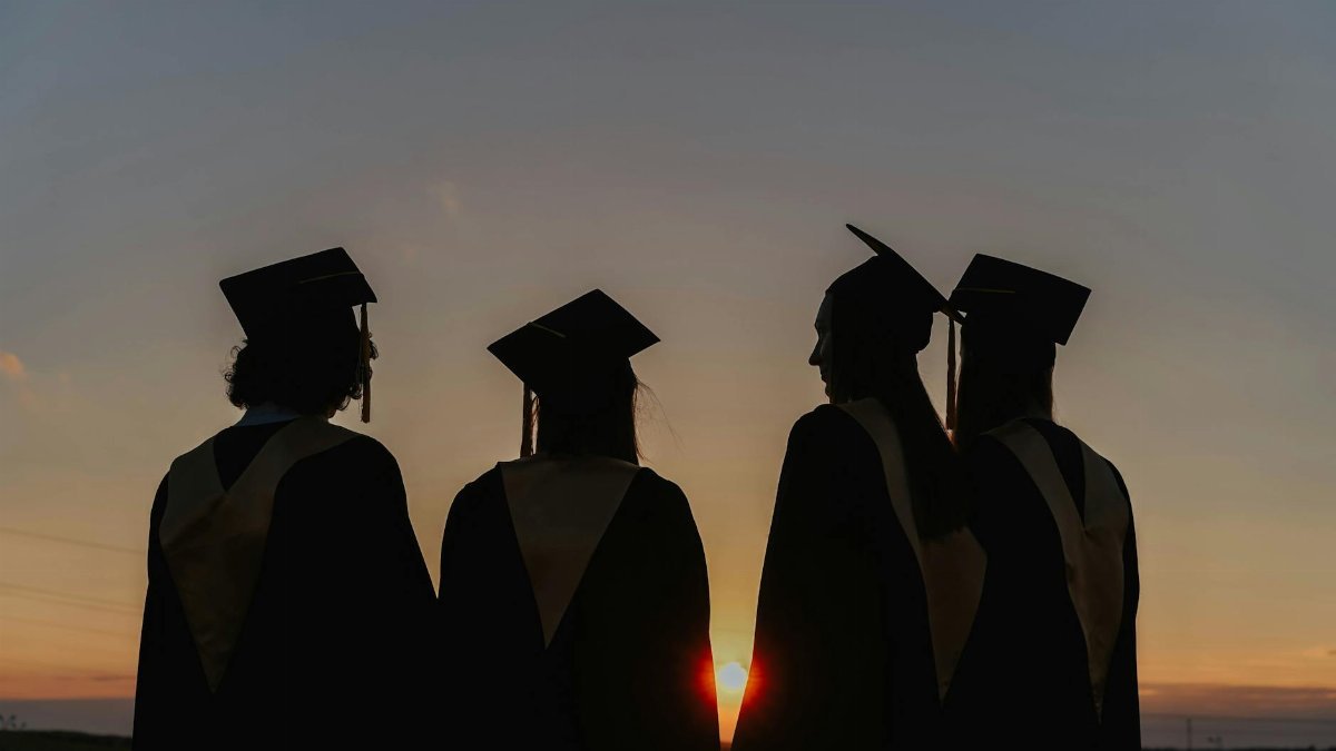 A group of graduates in caps and gowns silhouetted against a beautiful sunset, symbolizing achievement.