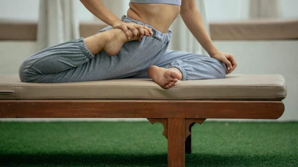 Side view of crop anonymous flexible female in sportswear performing Eka Pada Raja Kapotasana pose on bench during yoga session