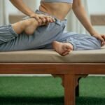 Side view of crop anonymous flexible female in sportswear performing Eka Pada Raja Kapotasana pose on bench during yoga session
