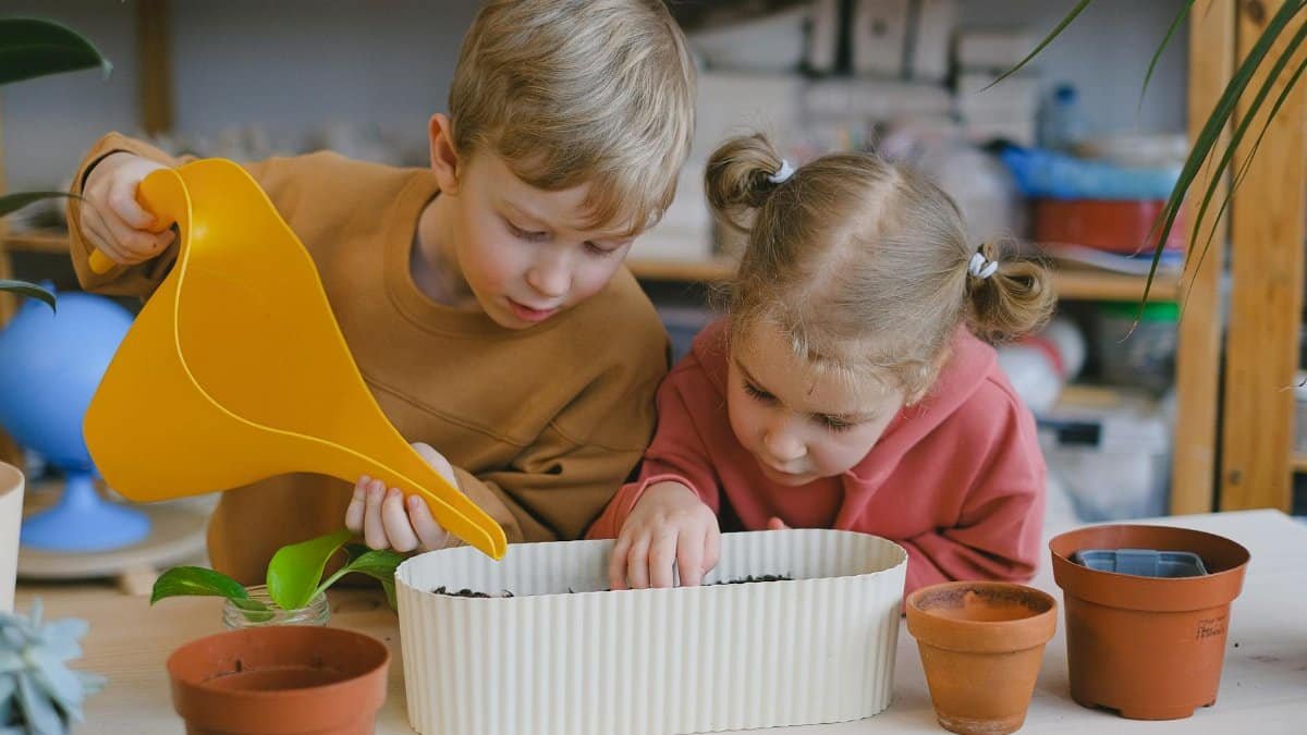 Two children planting seeds in pots indoors, learning about gardening and nature.