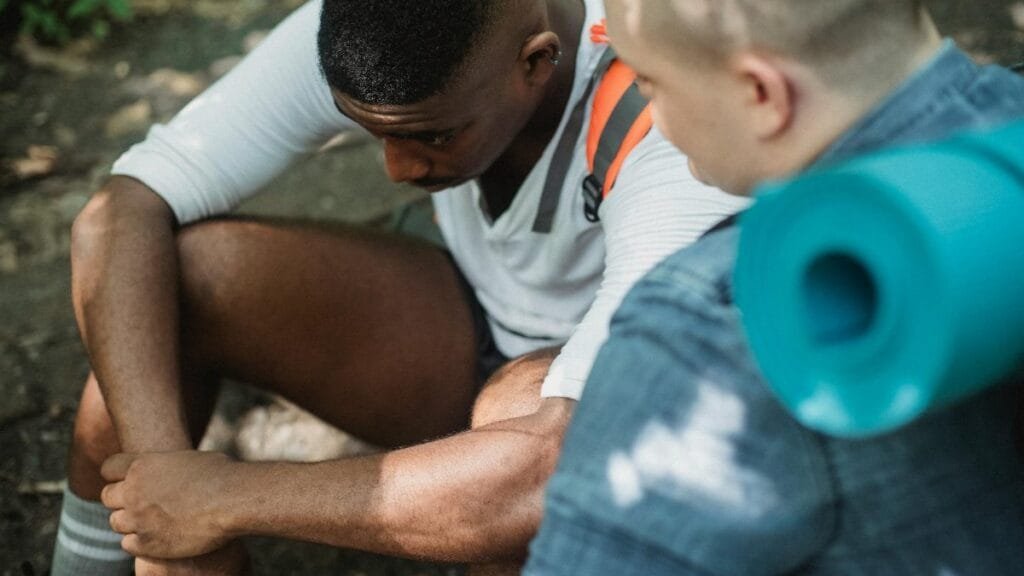 From above of tired African American male hiker having break in trekking with friend in woods