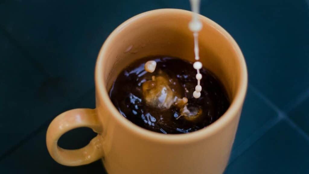 Close-up shot of cream being poured into a steaming hot cup of coffee.