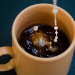 Close-up shot of cream being poured into a steaming hot cup of coffee.