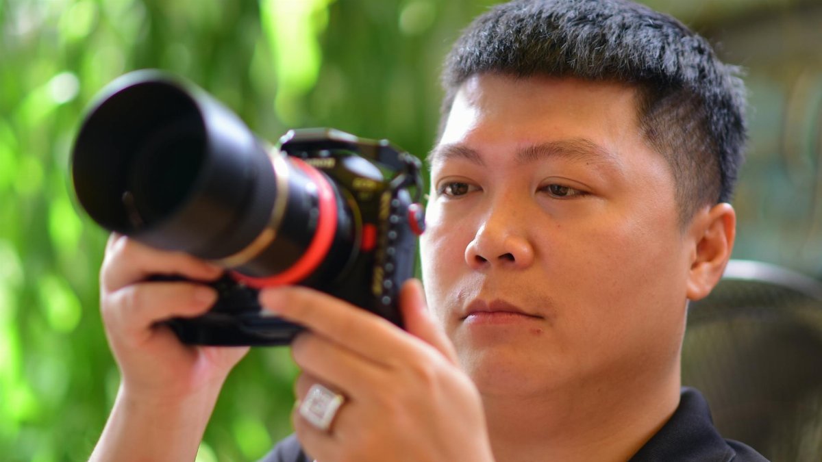 Man adjusting camera settings indoors with focus on lens and background blur.