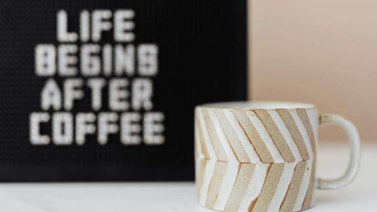 A ceramic coffee mug and motivational board saying 'Life Begins After Coffee' in a modern indoor setting.