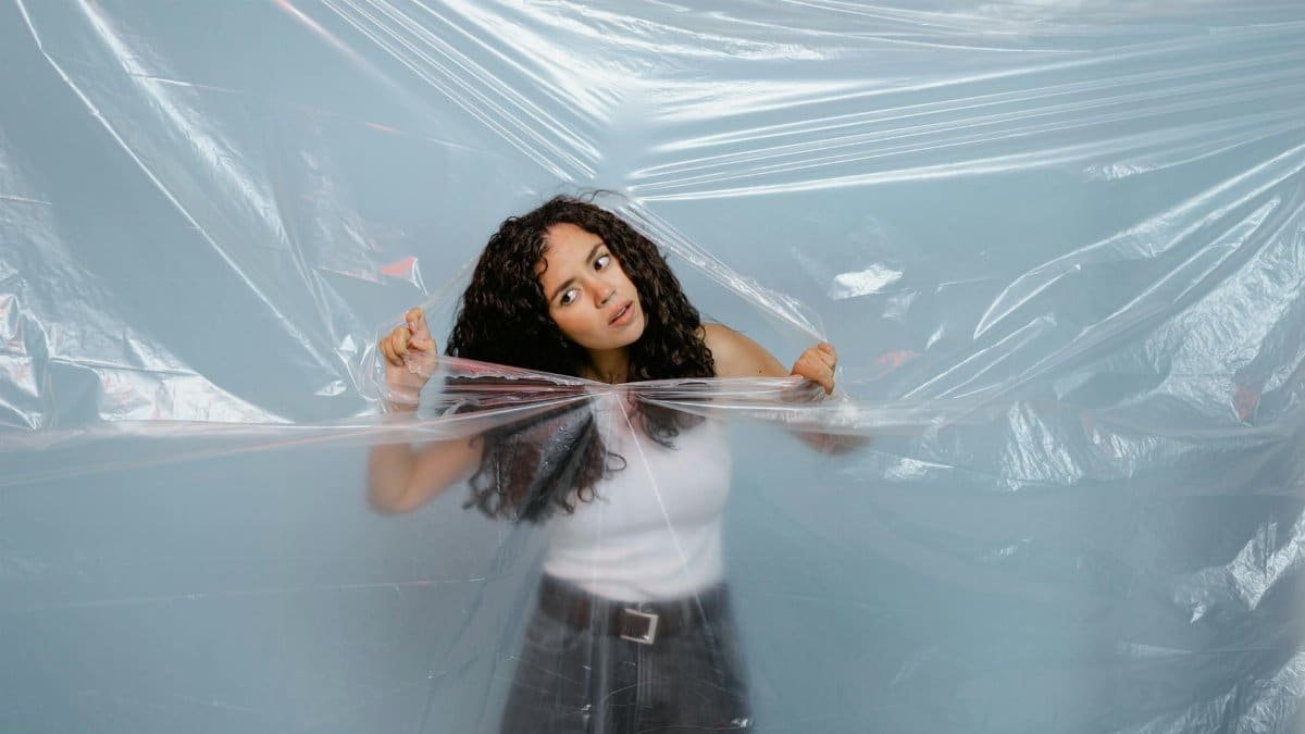 A woman tearing through a plastic sheet on a blue background, symbolizing freedom.