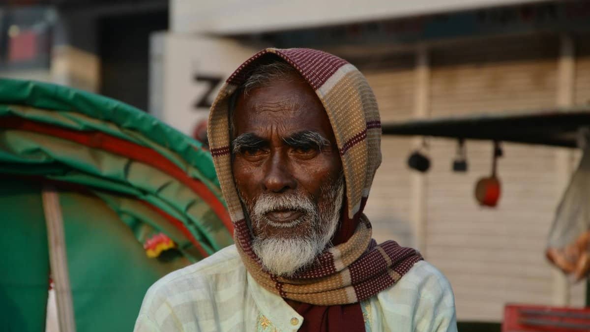Portrait of an elderly man wearing a headscarf in a bustling outdoor environment.