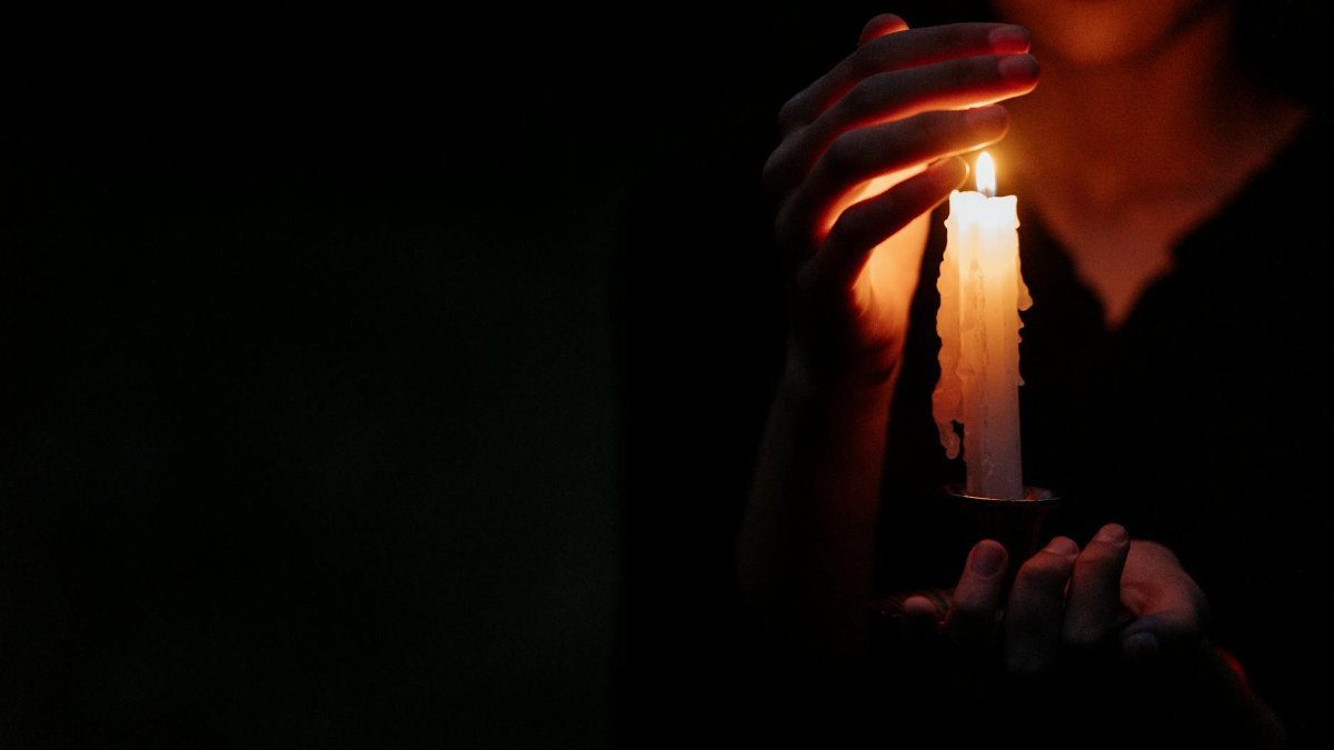 Close-up of a person in the dark holding a single lit candle, creating a moody atmosphere.