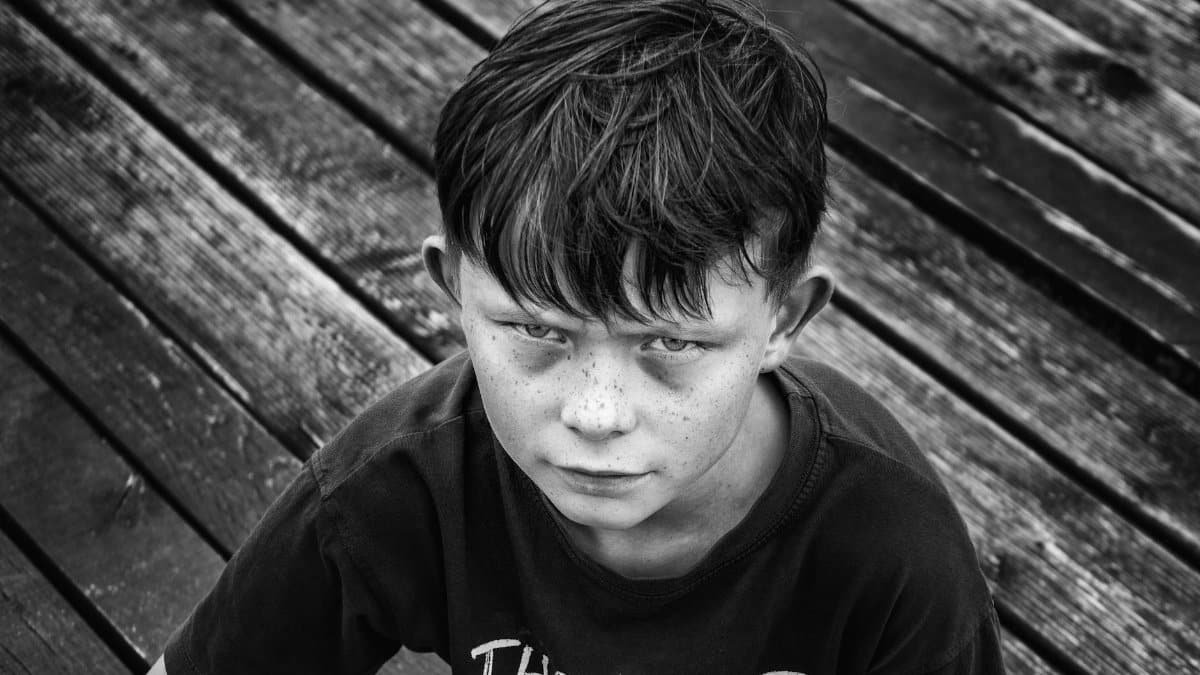 Monochrome portrait of a freckled boy on a wooden deck, conveying emotion.