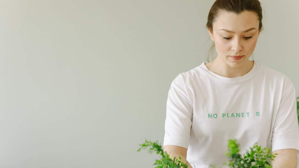 Young woman in 'No Planet B' shirt caring for indoor plants, promoting eco-consciousness.