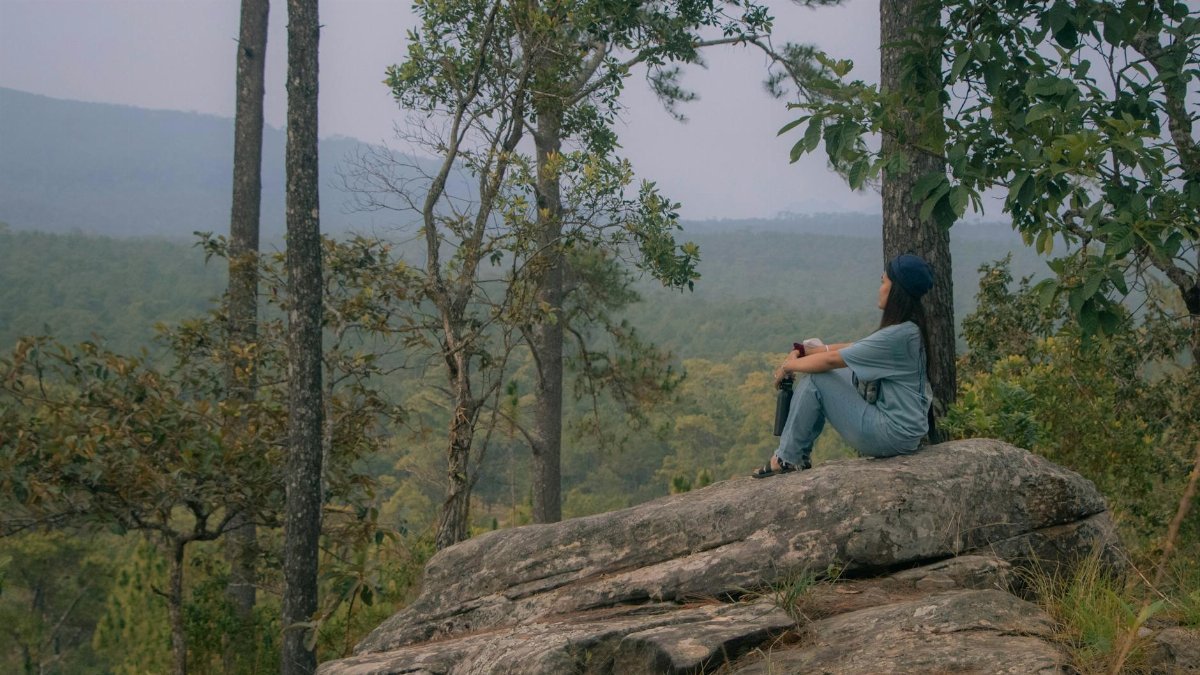 Peaceful scene of a woman seated on a cliff, enjoying nature's beauty.