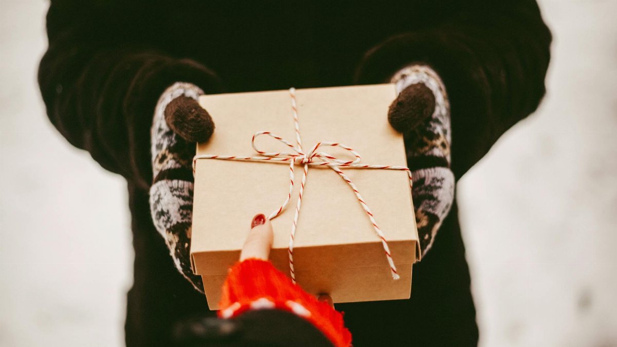 Warm winter scene of gloved hands exchanging a neatly wrapped gift outdoors.