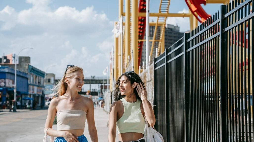 Two friends walking and talking at an amusement park on a sunny day, enjoying their time together.