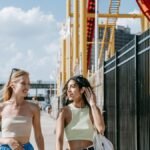 Two friends walking and talking at an amusement park on a sunny day, enjoying their time together.