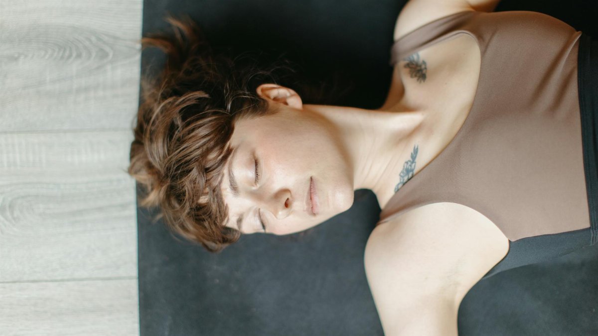 Woman lying on a yoga mat indoors with eyes closed, conveying relaxation.