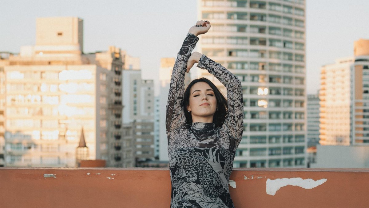 Woman stretching on a rooftop with a city skyline backdrop during the day.