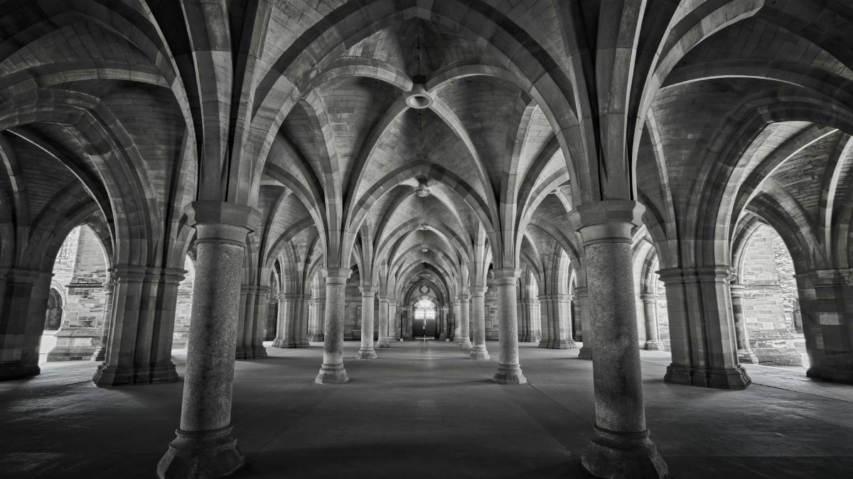 Monochrome view of the Gothic cloisters showcasing stunning arches and symmetry at the University of Glasgow, Scotland.
