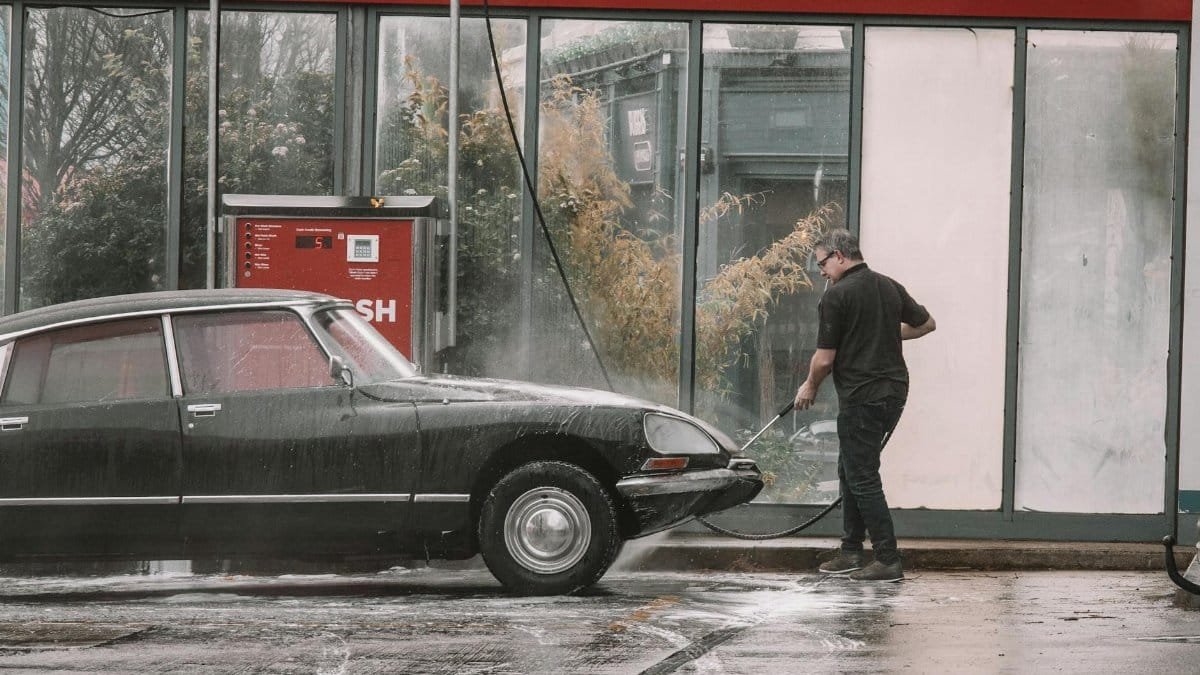 A man cleaning a classic car using a jet wash at an outdoor car wash in Dublin, Ireland.