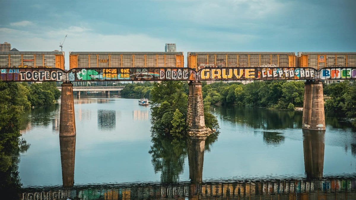A vibrant train bridge with graffiti over a river in Austin, Texas, showcasing urban artistry.