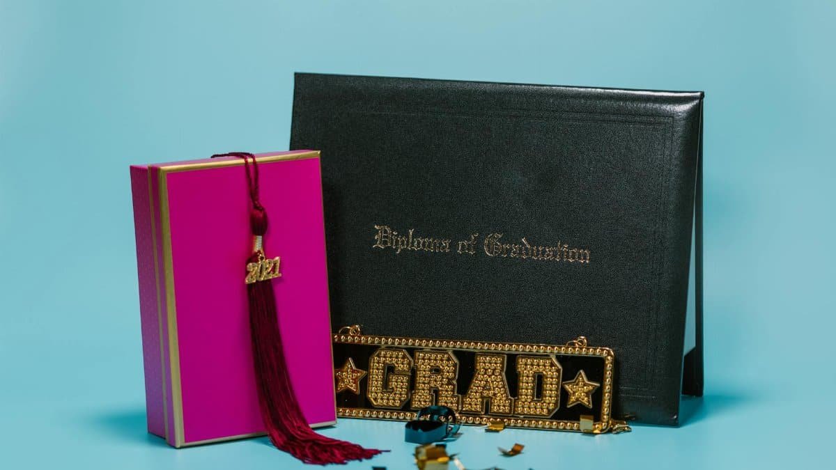Close-up of a graduation setup with diploma, tassel, and decorative elements on a teal background.