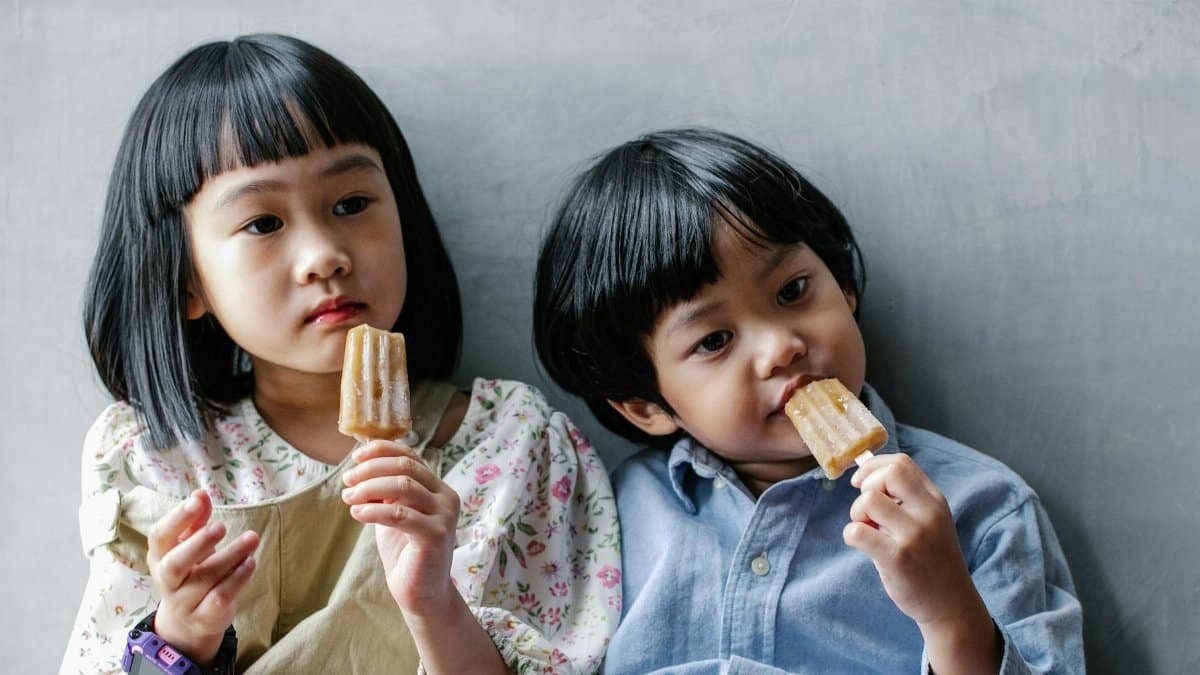 Cute moment of two children enjoying popsicles indoors, capturing childhood fun and friendship.