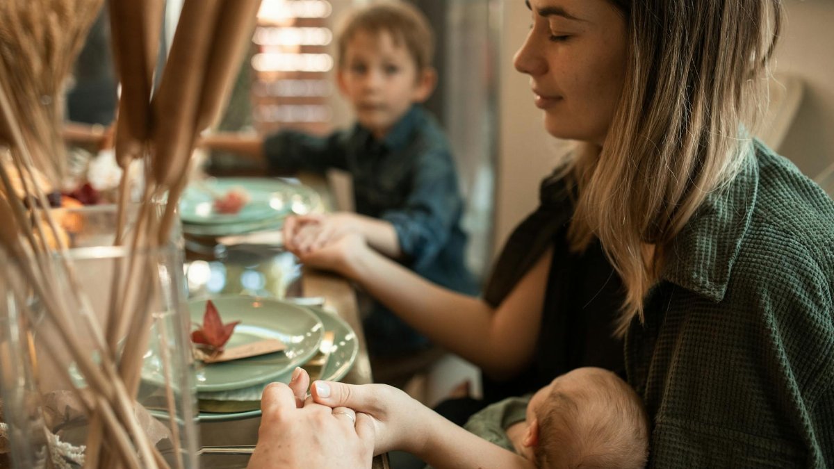 A family gathered indoors sharing a meal and holding hands during Thanksgiving.