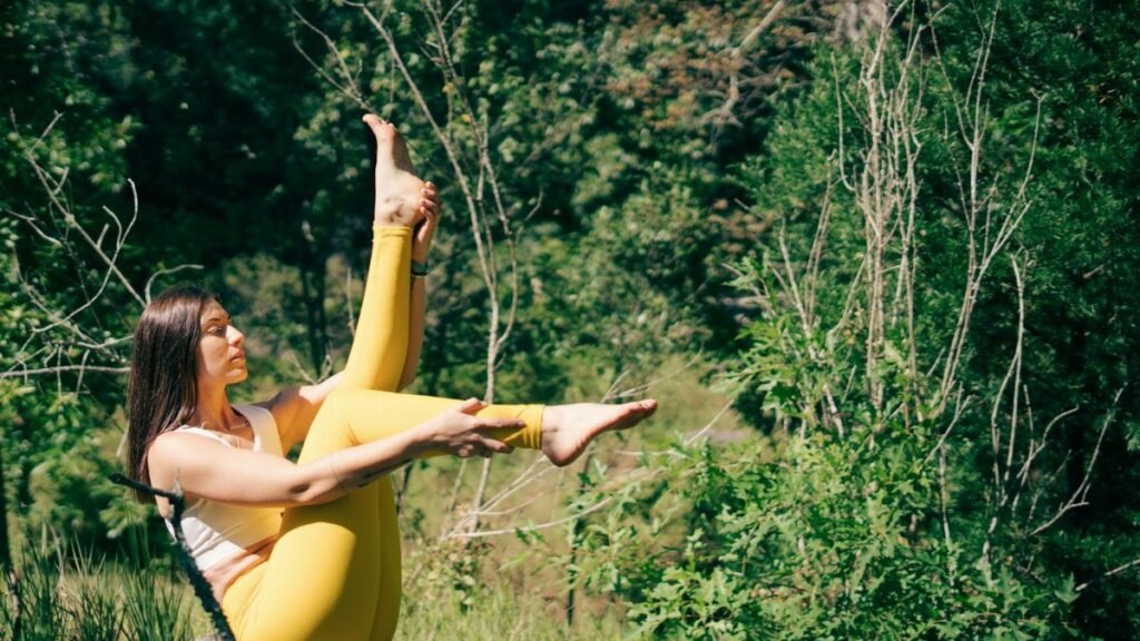 A woman in yellow leggings practices yoga outdoors surrounded by lush greenery.