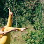 A woman in yellow leggings practices yoga outdoors surrounded by lush greenery.