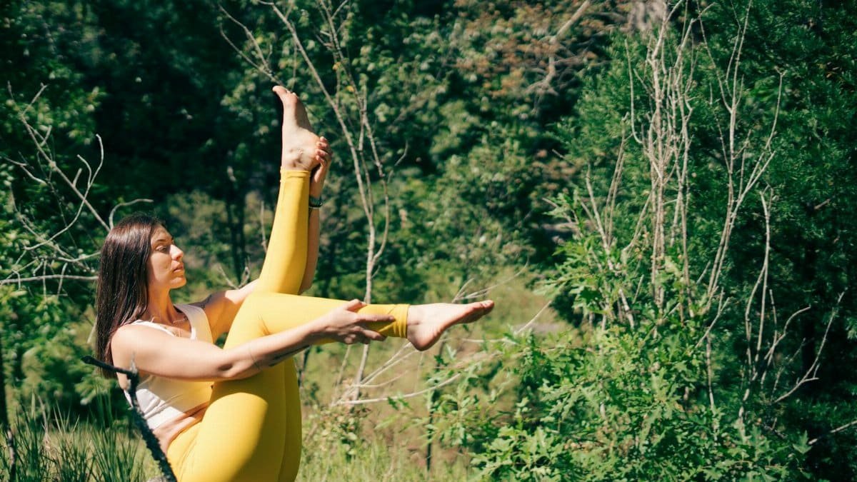 A woman in yellow leggings practices yoga outdoors surrounded by lush greenery.