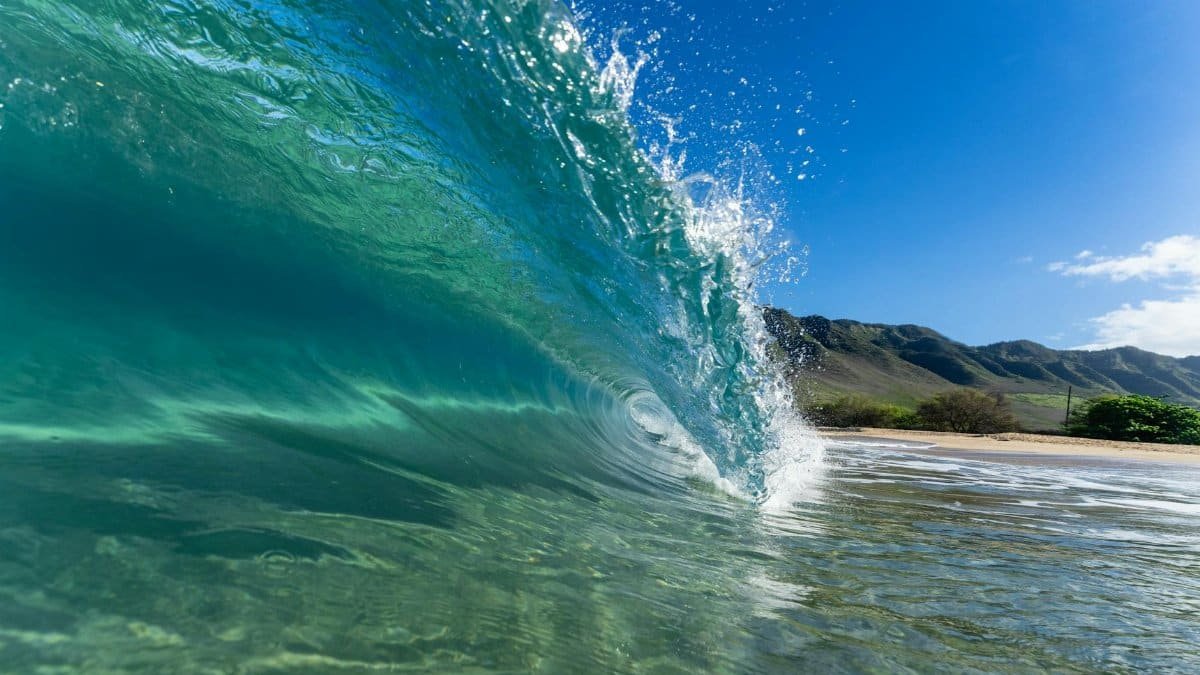 Close-up of a vibrant ocean wave crashing on a sunny beach with clear blue sky.