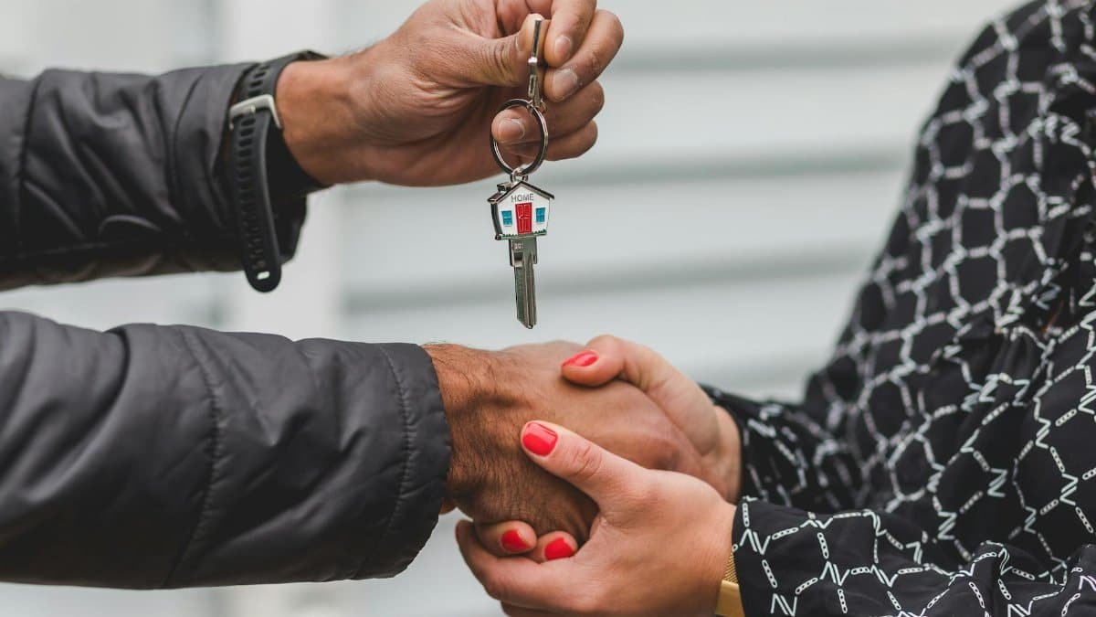 Close-up of a realtor handing over a house key to a new homeowner, symbolizing ownership and investment.