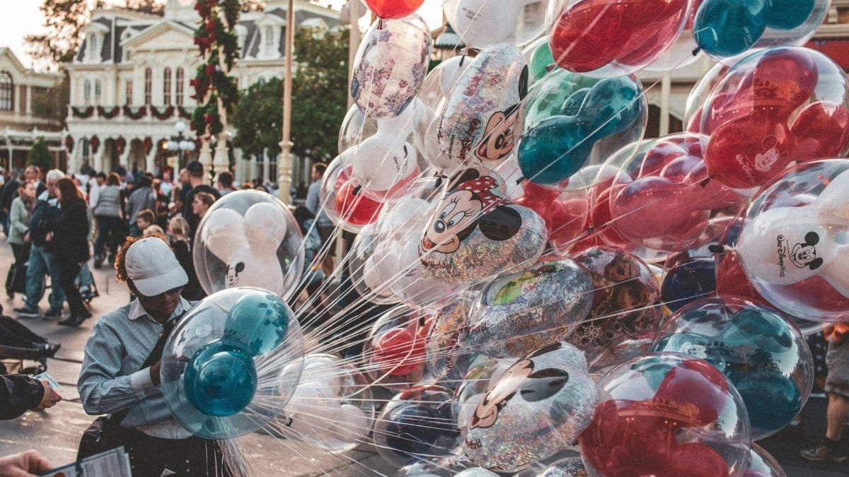 Colorful Mickey and Minnie balloons at a bustling theme park street.