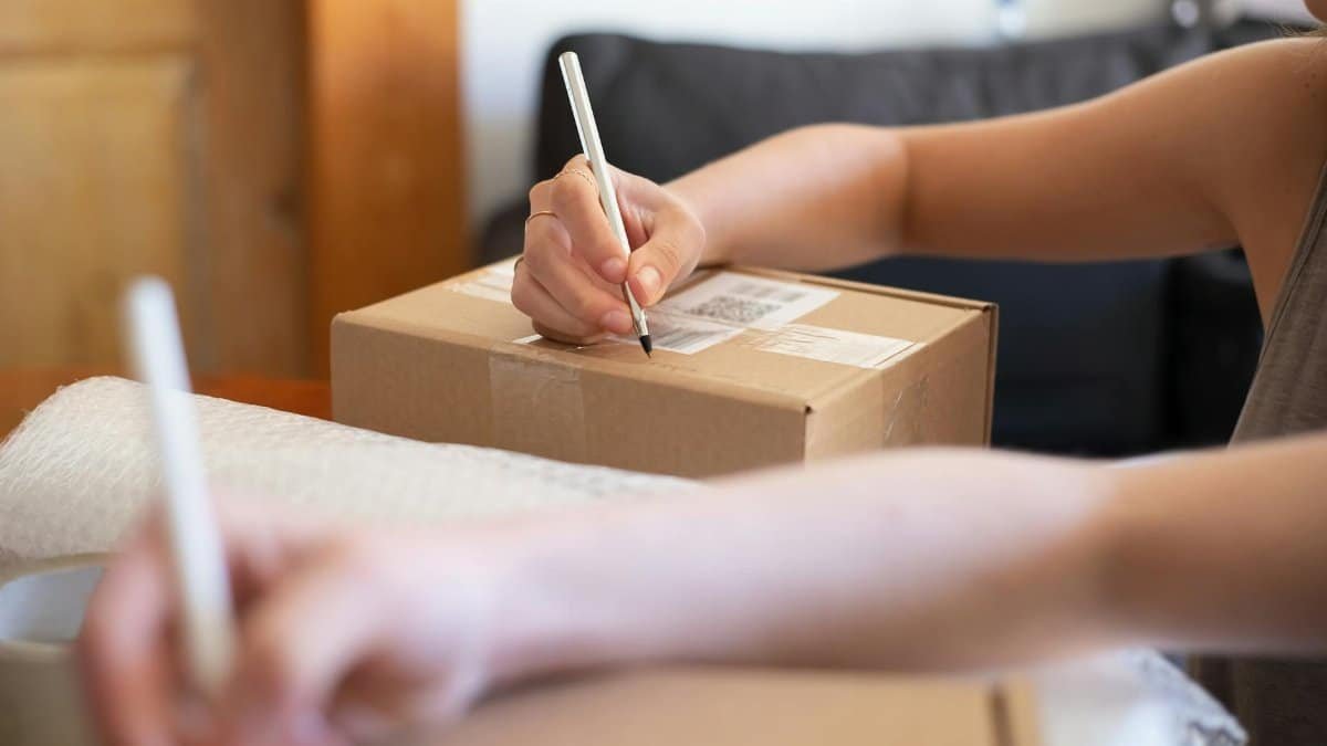 Close-up of hands labeling a cardboard box for online shipping from a home office.