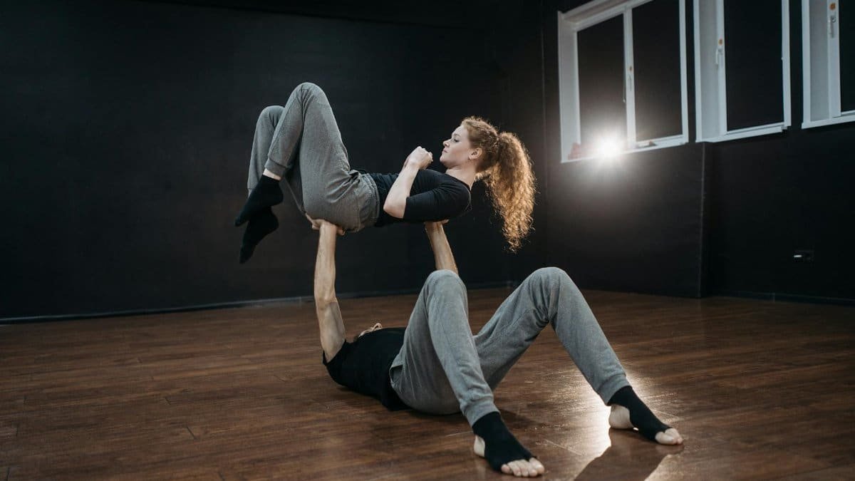 Two dancers performing acrobatic lift on a wooden floor in a studio.