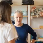 An instructor confidently engages with a student in a yoga studio setting, surrounded by equipment.