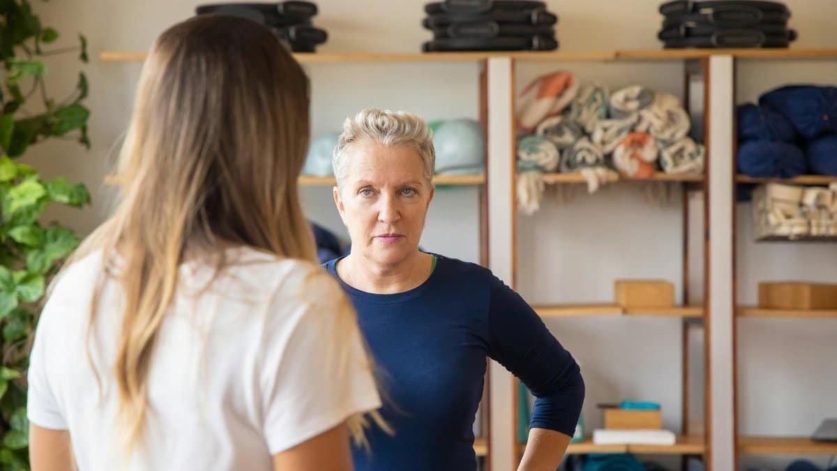 An instructor confidently engages with a student in a yoga studio setting, surrounded by equipment.