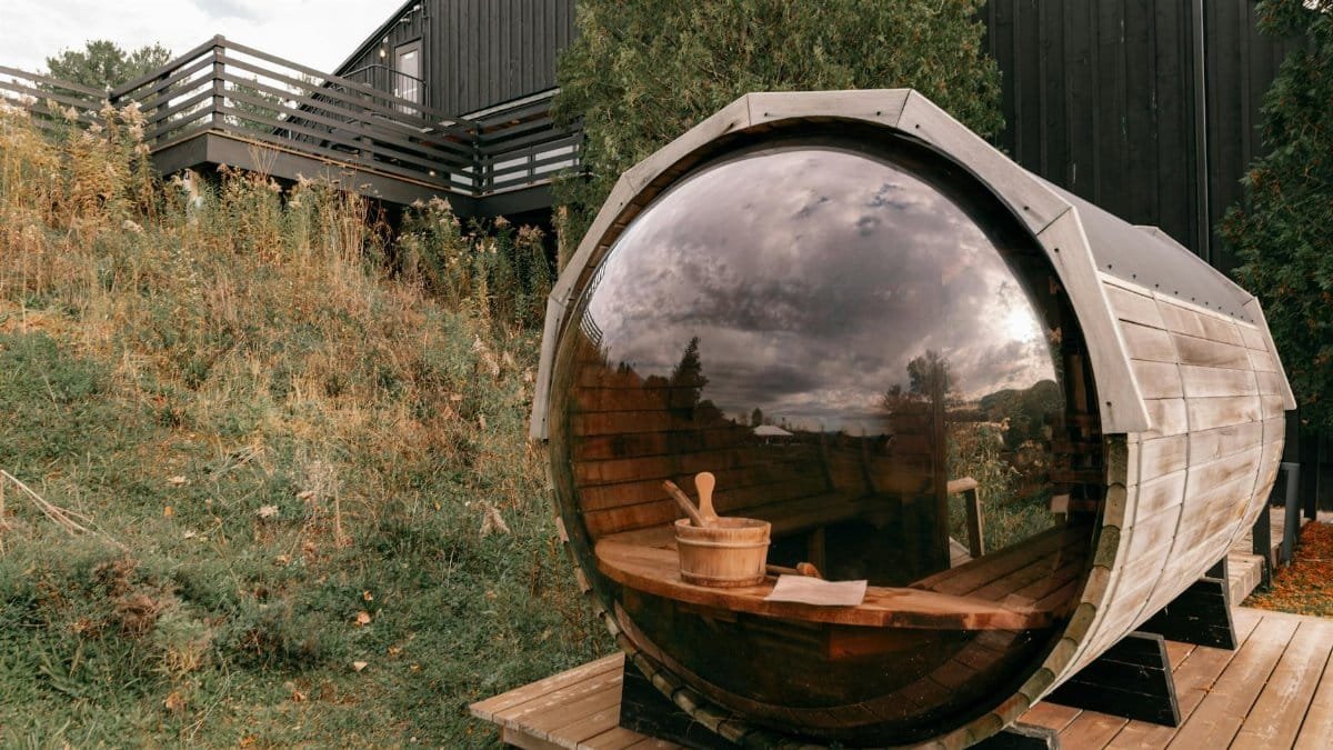 Rustic barrel sauna with glass front set in natural landscape, perfect for relaxation.