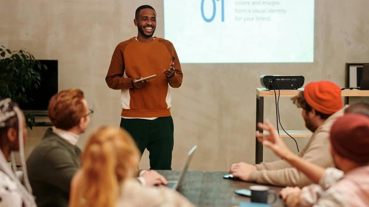 A man delivers a presentation in a modern office to a diverse group of colleagues.