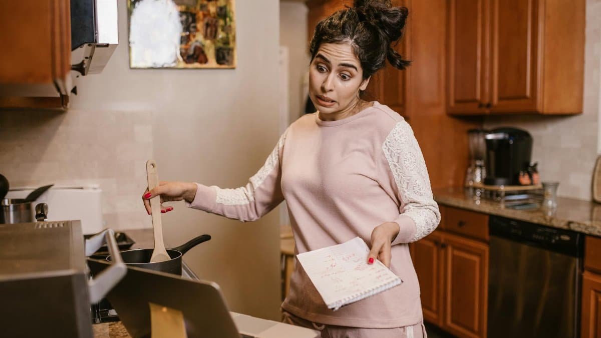 Woman multitasking in her kitchen with a laptop and notebook, cooking and working from home.