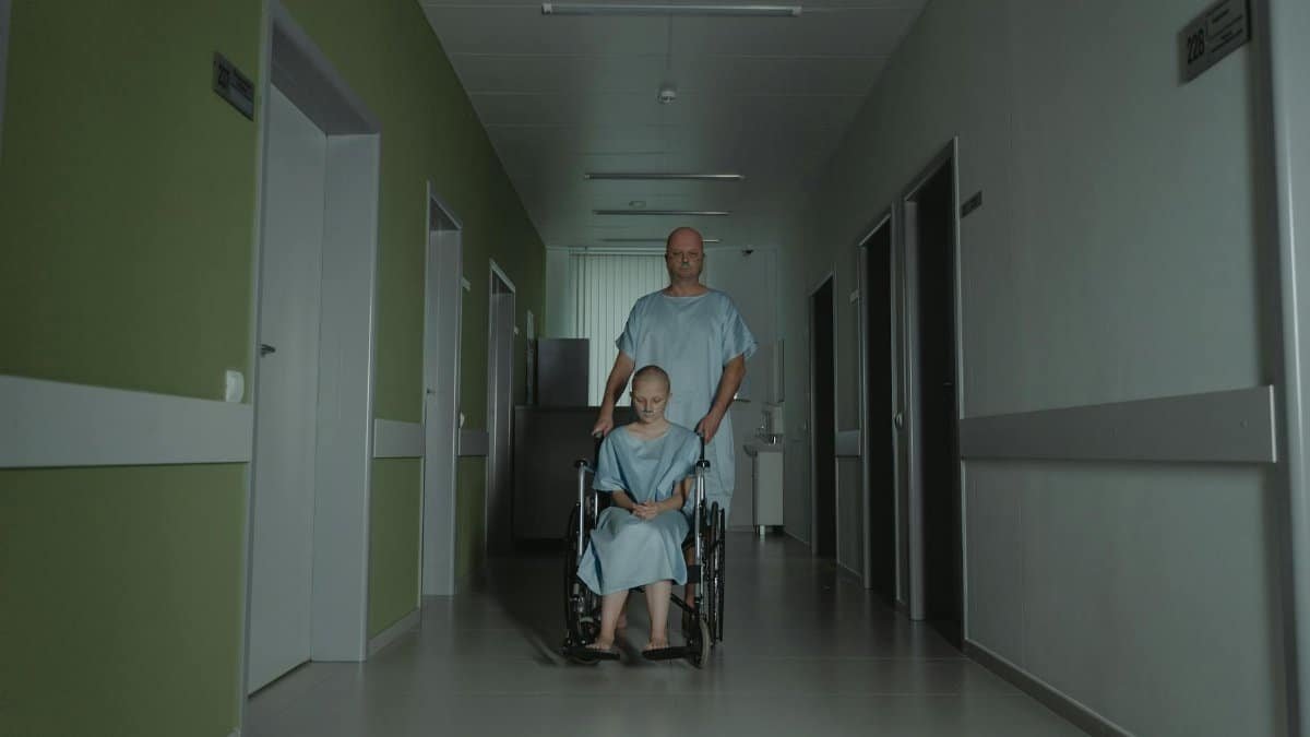Two patients in hospital gowns navigate a hallway, symbolizing struggle and resilience.