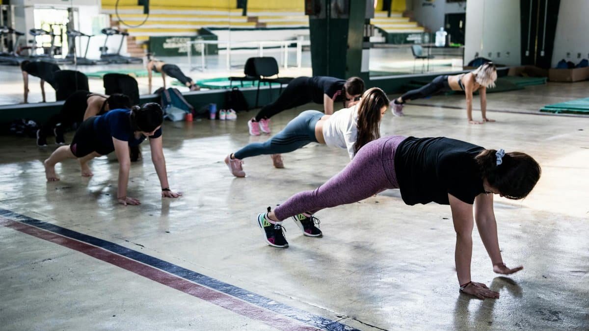 Group of women doing push-ups in a gym reflecting in a mirror.