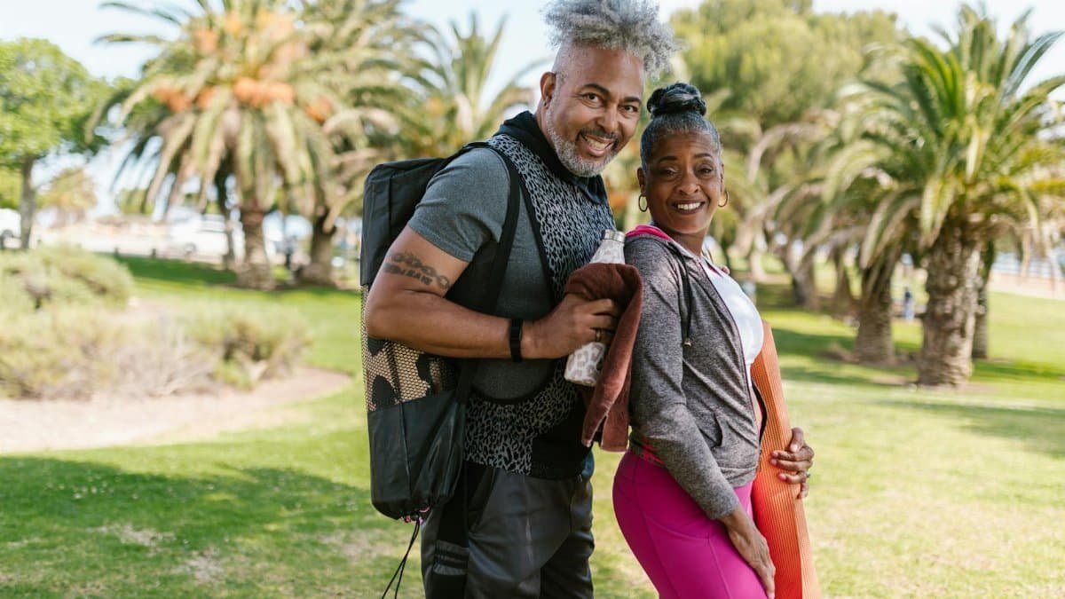 Happy senior couple practicing yoga outdoors in a park setting, promoting wellness and togetherness.