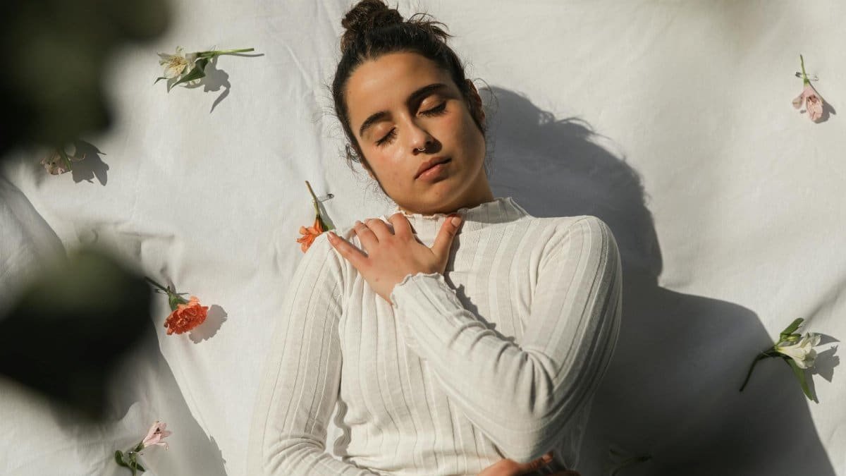 Serene woman with closed eyes in white sweater surrounded by flowers.