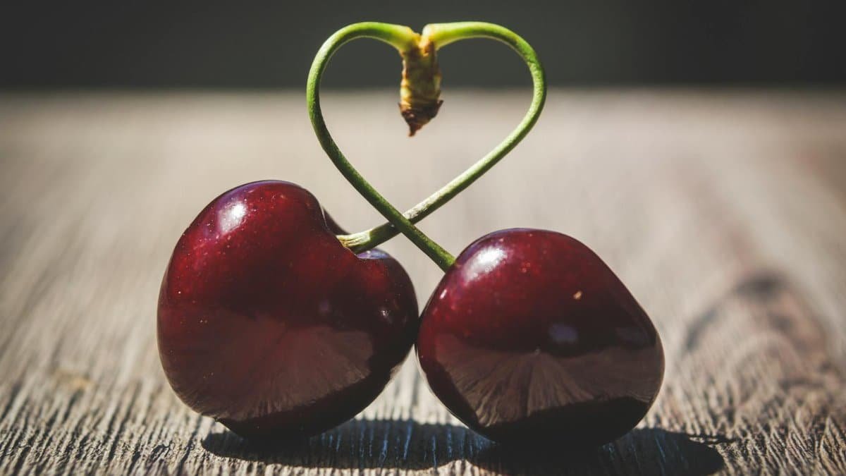 Close-up of two ripe cherries with heart-shaped stems on a wooden table, symbolizing love.